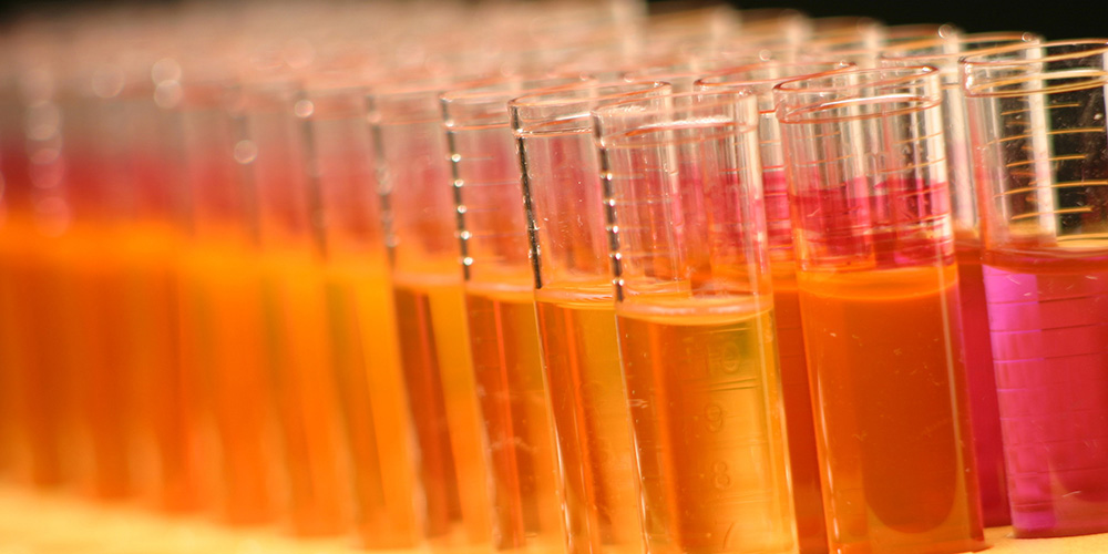 A row of test tubes containing liquids in shades of orange and pink.