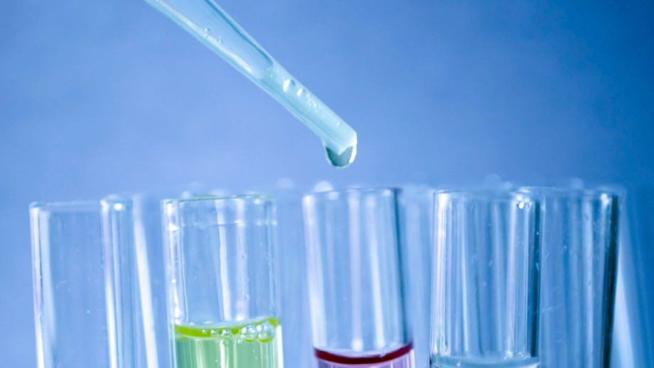 A pipette dispensing a liquid into a test tube among several other tubes with colorful liquids.