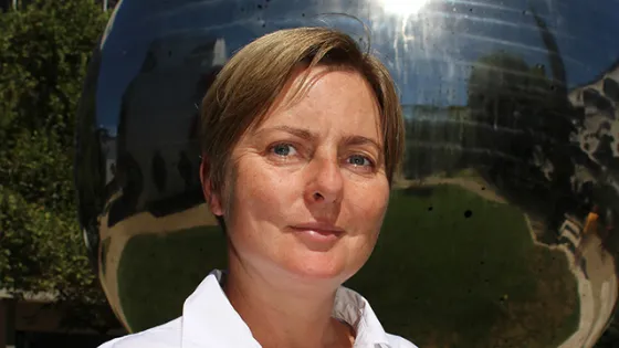A woman standing in front of a reflective spherical sculpture outdoors.