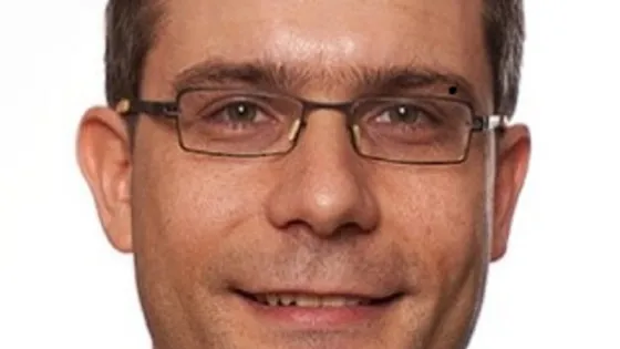 "Portrait of a smiling man wearing glasses and a gray shirt."