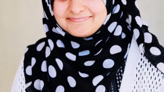 A woman smiling at the camera, wearing a black and white polka dot hijab.