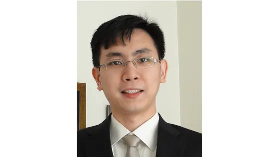 Portrait of a man in a black suit and tie, wearing glasses, with a neutral expression.