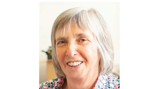 A smiling elderly woman with short gray hair wearing a floral shirt.