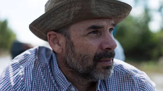 A man in a bucket hat and checkered shirt looks to the side thoughtfully.