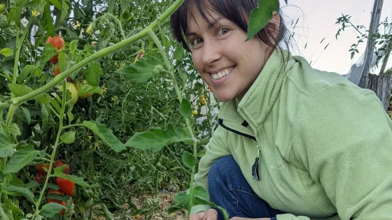 A woman smiling at the camera while crouching in a tomato garden.