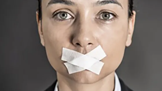 A woman in a business suit with her mouth sealed shut with pieces of tape.