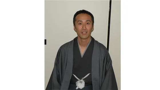 A man in traditional Japanese attire standing in front of a plain background.