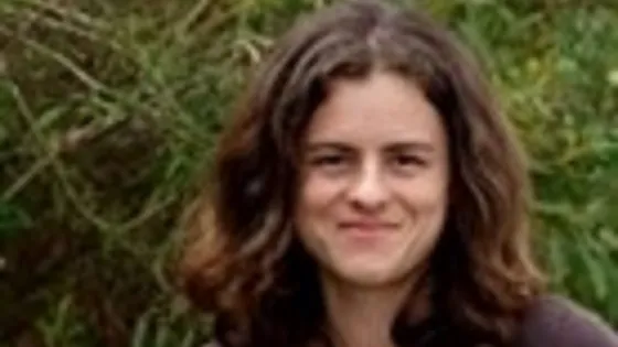 A woman smiling at the camera with a green, leafy background.