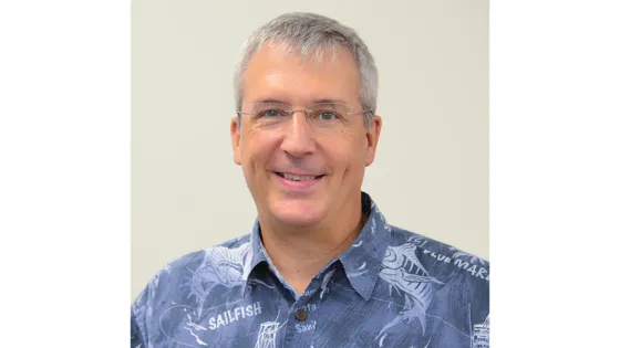 A smiling man wearing glasses and a blue fish-patterned shirt against a light background.