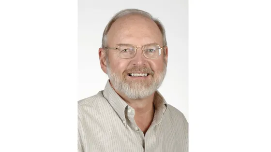 A portrait of an elderly man with a beard and glasses, smiling against a white background.