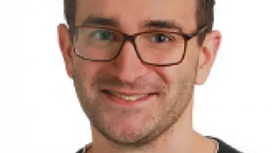 Portrait of a smiling man with glasses wearing a black shirt.