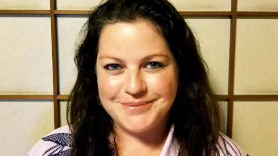 A woman with curly hair smiling in front of a traditional Japanese shoji screen.