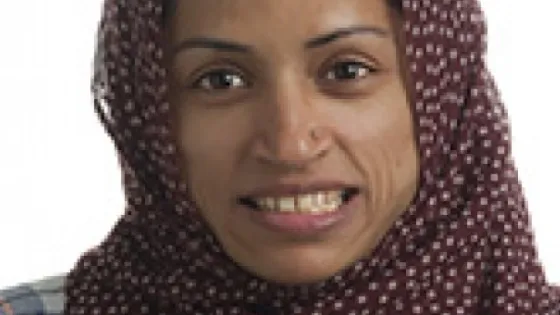 A woman wearing a burgundy hijab with a small print smiles gently at the camera.