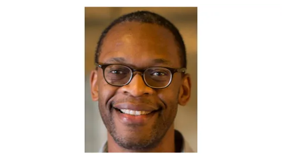 A portrait of a smiling man with glasses wearing a white shirt.