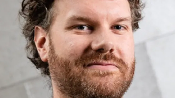 Portrait of a man with curly hair and a light beard, smiling slightly at the camera.