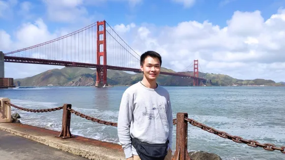 A man standing in front of the Golden Gate Bridge on a sunny day.