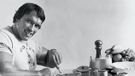 A man smiling while cooking in a kitchen with various ingredients and utensils spread out on the counter.