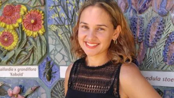 A woman smiling at the camera in front of a colorful floral mosaic wall.