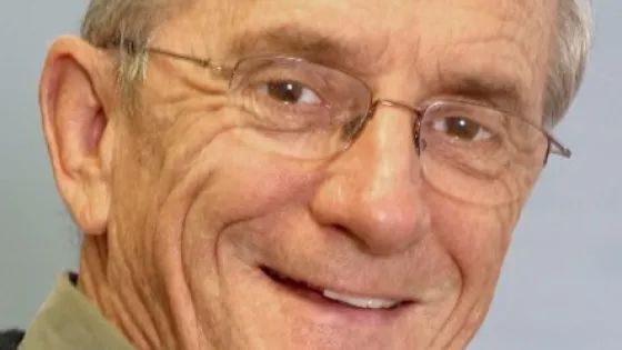 Portrait of an elderly man with glasses, smiling at the camera.