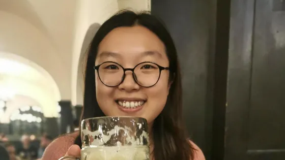 A woman in glasses smiles while holding a large beer mug at a table with traditional German food.