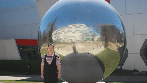 A woman stands in front of a large reflective sphere outside a modern building.