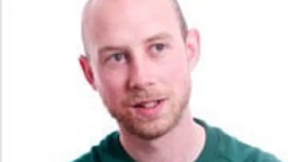 A portrait of a smiling bald man wearing a green shirt.