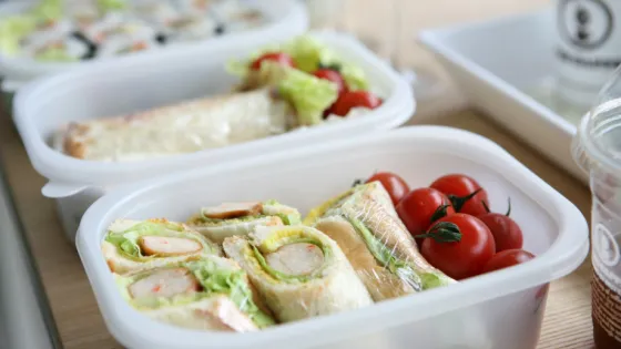 Plastic containers with assorted fresh wraps and cherry tomatoes on a wooden table.