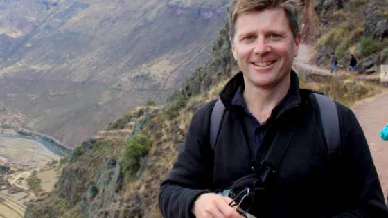 A man smiling at the camera with a mountainous landscape in the background.