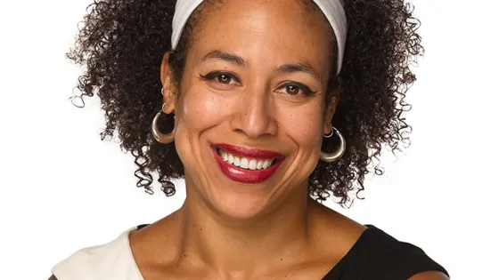 Portrait of a smiling woman with curly hair wearing a white headband, red lipstick, and hoop earrings.