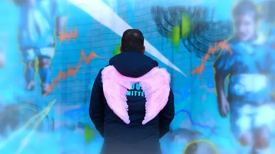 A man wearing a jacket with pink wings on the back is viewing an abstract digital display featuring blurred images of soccer players.