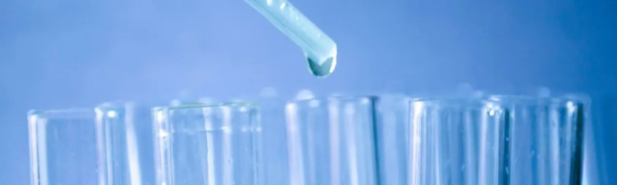 A pipette dispensing a liquid into a test tube among several other tubes with colorful liquids.