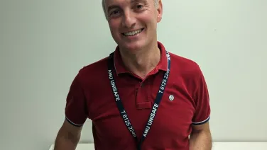A smiling man in a red polo shirt and a lanyard standing in an office setting.
