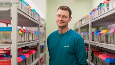 A man smiling in a storage room with shelves filled with colorful file folders.