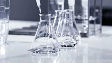 Several laboratory flasks with clear liquid on a white reflective surface in a scientific laboratory.