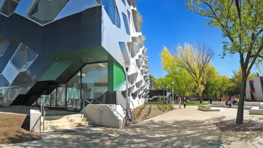 Panoramic view of a modern university campus with distinctive, geometrically designed buildings and a tree-lined pedestrian pathway.